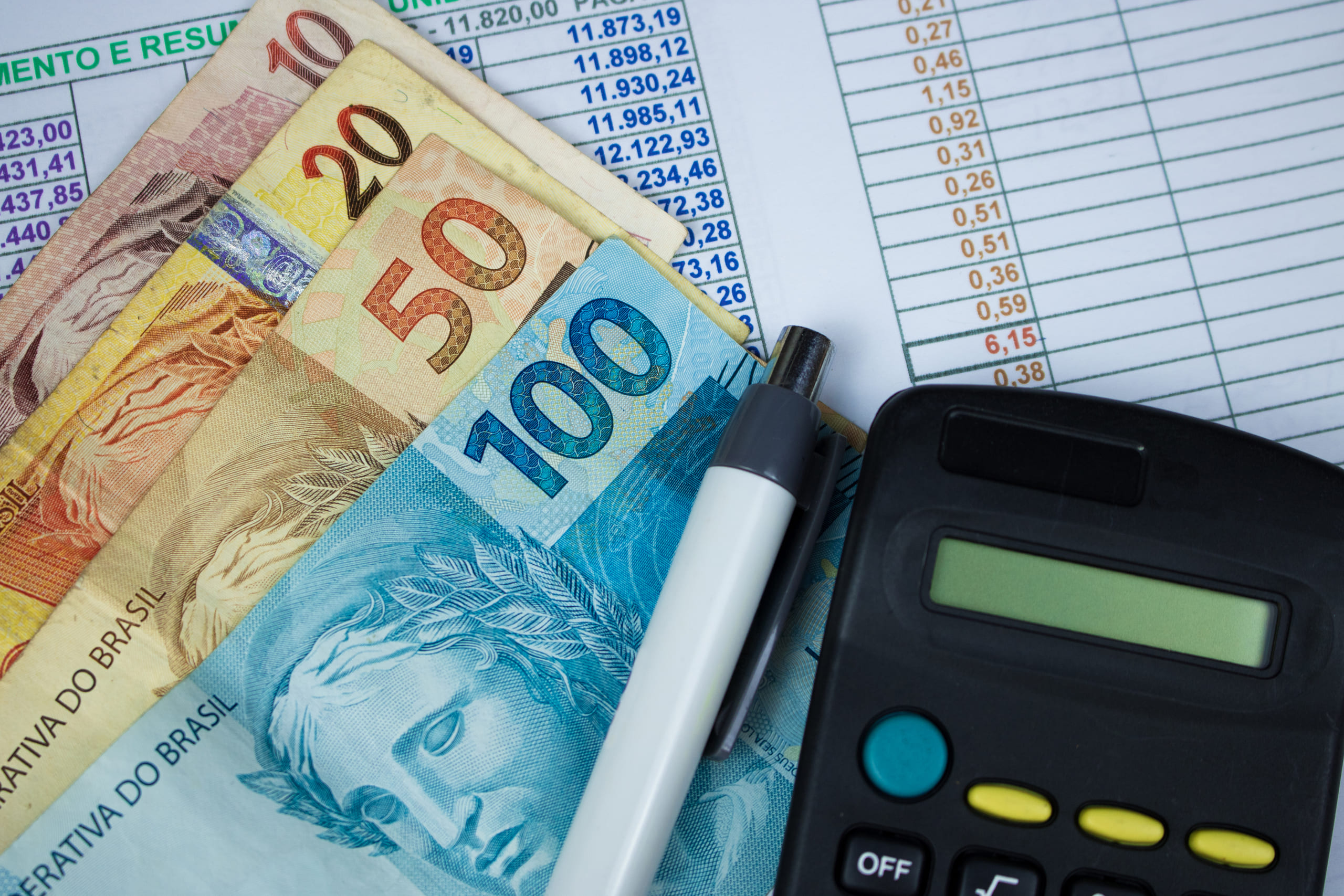 Cédulas de real, calculadora e planilha representando a influência da taxa Selic no mercado financeiro brasileiro