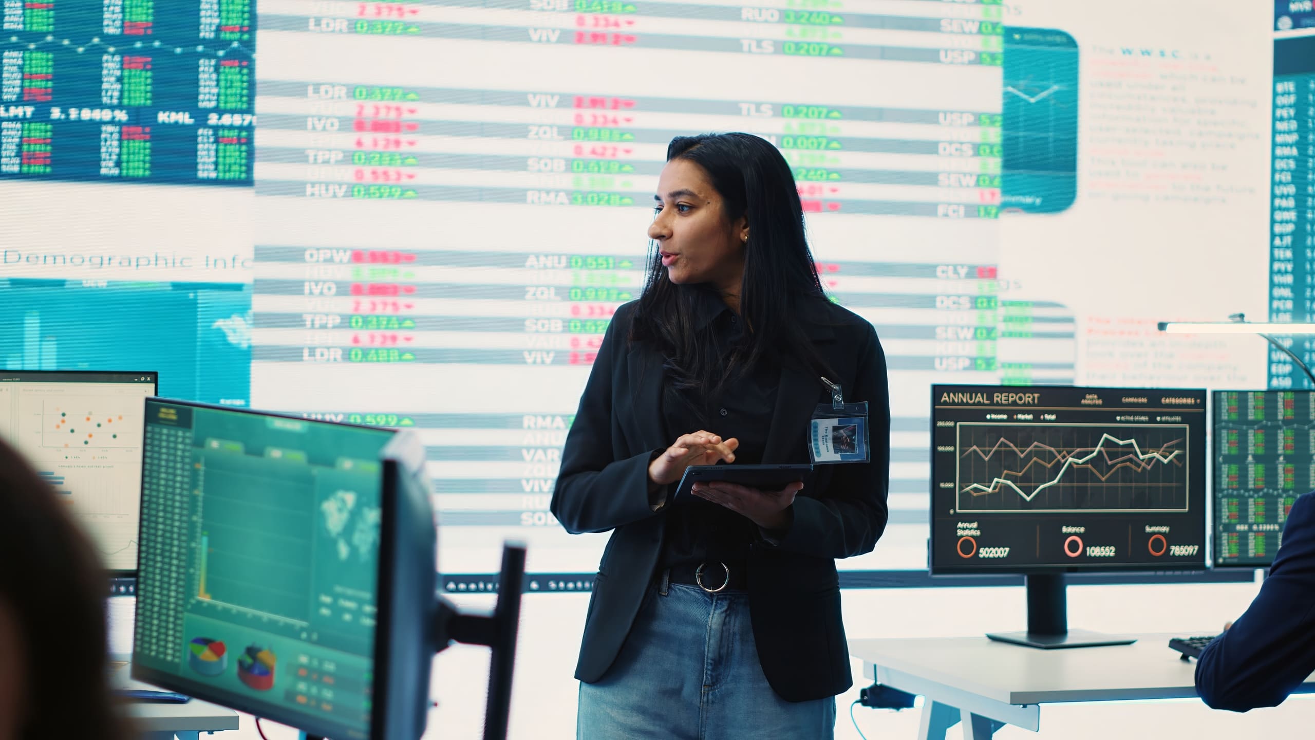 Profissional analisando gráficos financeiros em ambiente corporativo com múltiplos monitores exibindo dados de mercados emergentes.