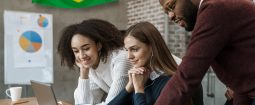 Profissionais analisando dados econômicos em um notebook em escritório com bandeira do Brasil ao fundo, representando o mercado de trabalho e indicadores de emprego.